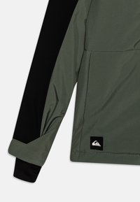 Giacca verde e nera con maniche lunghe, caratterizzata da una texture liscia, un design a mezza zip e una patch con logo in basso a destra.
