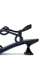 Sandalo con tacco alto di colore blu navy, decorato con anelli tempestati di cristalli e un design unico del tacco a campana. Il materiale appare morbido con una finitura lucida.