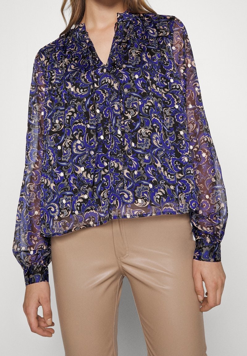 Haut blouson transparent avec un motif cachemire bleu et noir, encolure en V, manches longues et détails froncés aux épaules.