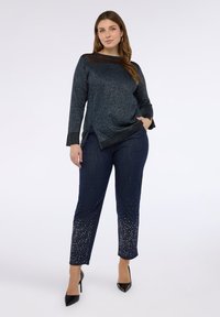 Marinblå tröja med texturerat tyg och mesh-detaljer, matchad med mörka denimbyxor med nitar vid fållen. Svarta klackar fulländar looken.