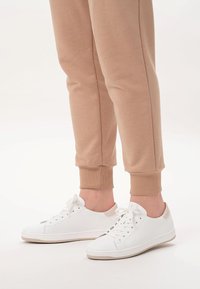 Białe sneakersy o gładkiej fakturze, z sznurowanym zapi ęciem i beżowym akcentem na pięcie. Połączone z beżowymi dresami z mankietami.