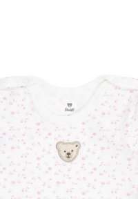 Un body de algodón blanco con patrones de flores rosas, que presenta un bordado de un oso beige en el pecho y cierres a presión en el cuello.