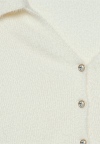 Tissu tricoté blanc doux avec un col replié et trois petits boutons ronds avec des centres en pierre précieuse claire.