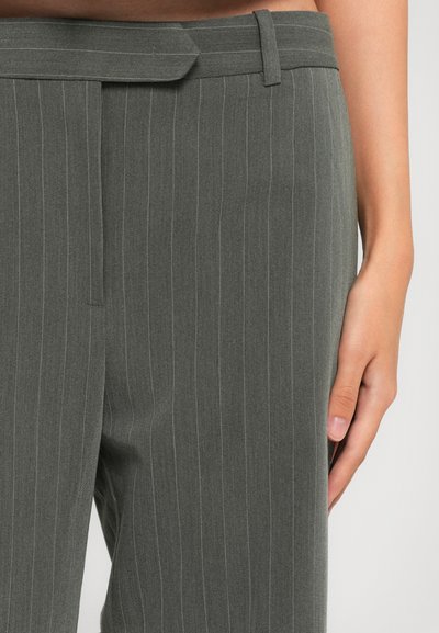 Gray pinstripe tailored pants with high waist and side belt loop, worn by a person standing with right hand by their side.