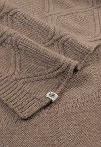 Beige knitted sweater with a textured diamond pattern, ribbed hem, and a woven tag. Made from soft, thick yarn.