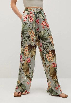 Spodnie o szerokich nogawkach z tropikalnym kwiatowym wzorem w zielonych, różowych i żółtych odcieniach, noszone z beżowym, krótkim topem i sandałami.