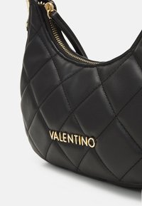 Quilted black leather handbag featuring a gold "Valentino" logo. The bag has a zip closure and a curved shape with a smooth texture.