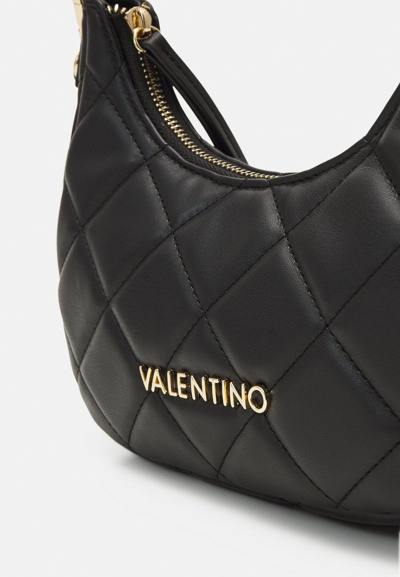 Sac à main en cuir noir matelassé avec un logo doré "Valentino". Le sac dispose d'une fermeture éclair et a une forme incurvée avec une texture lisse.