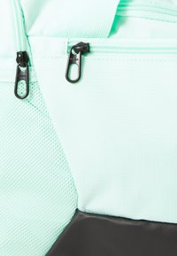 Mintgroene rugzak met een zachte mesh-stof aan één kant, aangevuld met een gladde zwarte basis en dubbele zwarte ritsen met branding.