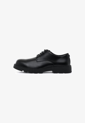 Zapato negro de cuero con cordones, con punta redondeada, suela de goma negra resistente y detalles de costura mínimos. Textura suave con un acabado pulido.
