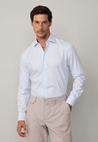 Camicia a righe azzurro chiaro in cotone, con colletto abbottonato, maniche lunghe e vestibilità slim. Abbinata a pantaloni beige chiaro.