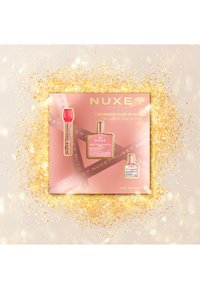 El set de regalo NUXE en una caja rosa presenta dos botellas: una botella cuadrada de vidrio con un producto de rosa y un tubo circular con tapa roja. Detalles en dorado.