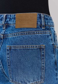 Középkék farmernadrág, puha tapintással. A derékpánton található barna bőrcímke "LAMANIA" felirattal, ami bele van nyomva. Klasszikus hátsó zsebkialakítás.