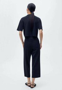 Un haut noir cropped à manches courtes associé à un pantalon noir à jambes larges, tous deux en tissu lisse. Modèle portant des sandales plates, vu de dos.