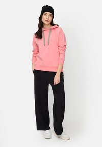Pink hoodie with gray drawstrings, relaxed fit, paired with black wide-leg pants and white sneakers. Black beanie completes the look.