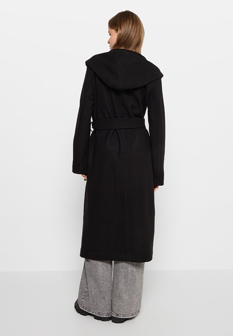 Svart lång kappa med huva, bälte i midjan, tillverkad av ett texturerat tyg. Har en rak siluett och vida ärmar.