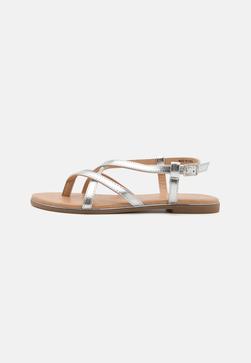 Silver metallic sandals with crisscross straps, a flat tan insole, and adjustable ankle strap; smooth texture and minimalist design.