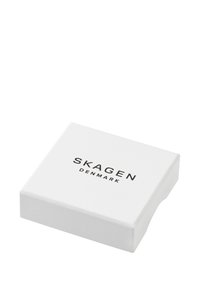 Bílé čtvercové balení s nápisem "SKAGEN DENMARK" v černé barvě, zaoblené hrany a hladký povrch. Minimalistický design, bez dalších akcentů.