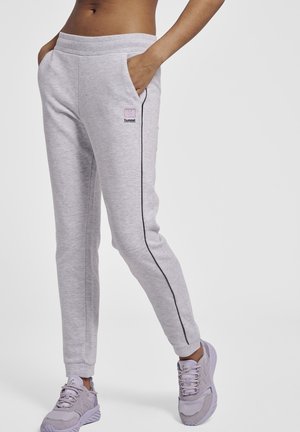Grå joggebukser med slim fit, lommer, sort sidepip og et lille lyserødt logo. Sat sammen med lyse lilla sneakers.