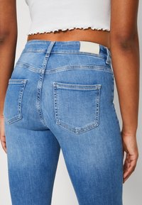 Blå denimjeans med hög midja, som har en jämn textur, två bakfickor och diskreta sömdekorationer, i en ljus tvätt.