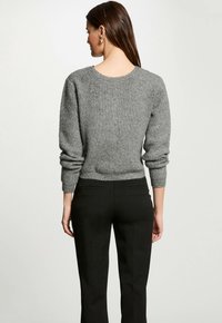 Grijs gebreid sweater met een ronde hals en opgerolde mouwen, gecombineerd met zwarte op maat gemaakte broek, die een gladde textuur en aangesloten silhouet laat zien.