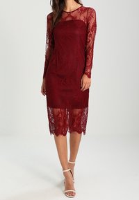 Burgundy lace dress with long sheer sleeves, a fitted bodice, and a scalloped hem, featuring intricate floral patterns and a smooth lining.