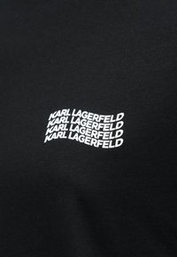 Μαύρο ύφασμα με το "KARL LAGERFELD" να επαναλαμβάνεται τέσσερις φορές σε λευκό, διατεταγμένο σε κυματιστό στοιβαγμένο μοτίβο κειμένου.