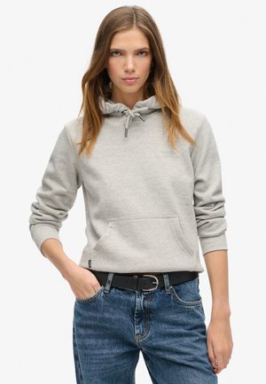 Lichtgrijze hoodie met een trekkoord, voorzien van een voorzak en geribde manchetten. Gecombineerd met blauwe denim jeans en een zwarte riem.