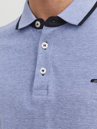 Lichtblauwe poloshirt met een gestructureerde stof, zwarte kraagaccenten, drie witte knoppen en een klein logo aan de zijkant.