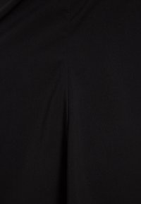 Schwarzer Stoff mit glatter Textur und einem vertikalen Schlitz. Das Material wirkt leicht und fällt weich, ohne sichtbare Muster.