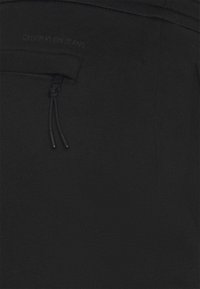 Černá textilie kalhot Calvin Klein Jeans s hladkým povrchem, s kapsou na zip a detaily v podobě tkaničky v pase.