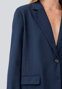 Navy blazer with a notched collar, single button closure, and front pocket. Soft fabric with a smooth texture.