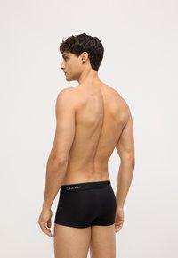 Crne bokserice s kontrastnim pojasom na kojem se nalazi logotip "Calvin Klein". Glatka tkanina, prilagodljiv dizajn i dužina do sredine bedara.