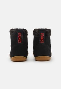 Botas negras de ante hasta el tobillo con un puño forrado de piel de animal y un logo rojo "CAMPER" en la parte trasera, que cuentan con una suela de goma beige.