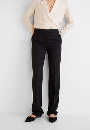 Mujer con blazer crema acanalado de doble botonadura, pantalones negros de corte recto y zapatos planos negros puntiagudos con detalle de lazo.