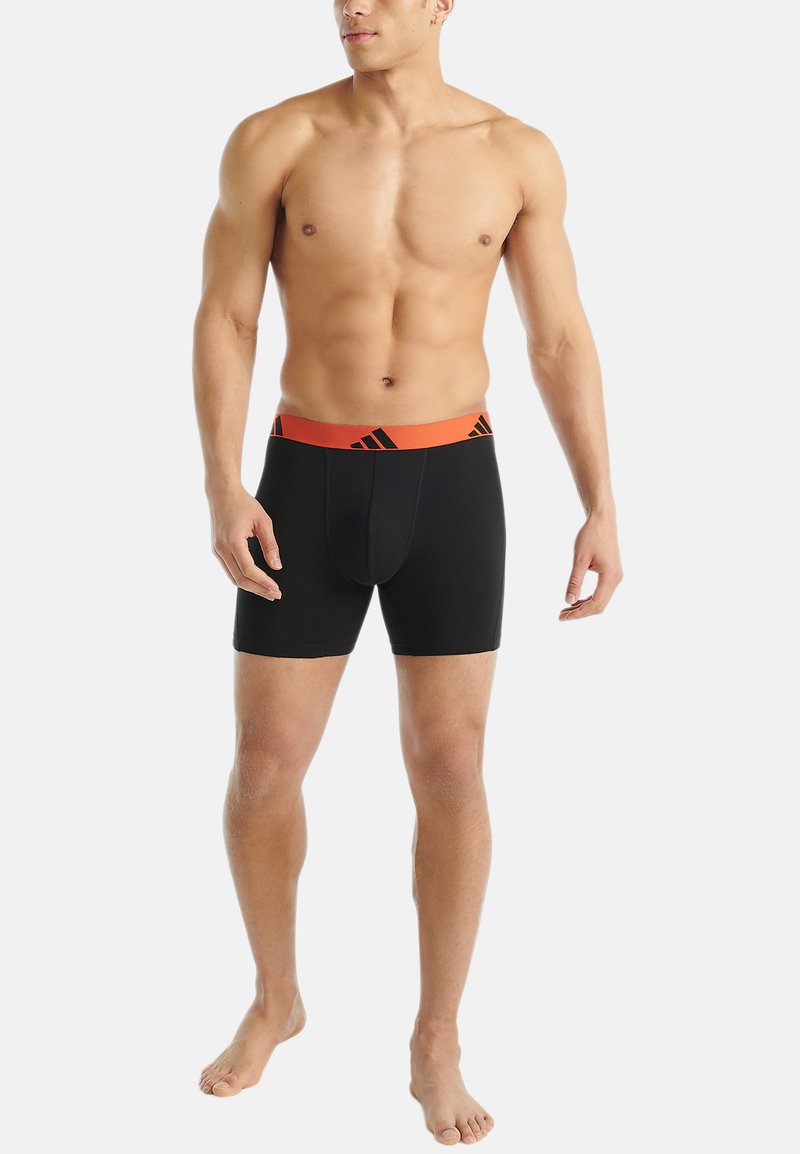 Svart boxertrosor med ett brett orange midjeband som har svarta ränder. Tyget ser slätt och åtsittande ut, utformat för komfort och stöd.