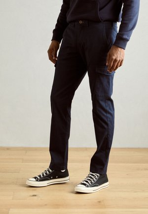 Navy cargo pants with a slim fit, made of cotton blend, featuring side pockets and paired with black high-top sneakers.