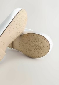 Ballerine bianche con finitura in raso e suole in gomma beige, con un motivo di stelle e scarpe da balletto sulla parte inferiore.