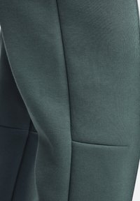 Gröna leggings i stretchtyg med en slät textur och en figurnära design, framhävda av en sidoficka och subtila sömdetaljer.