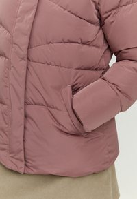 Padded jacket in mauve with quilted pattern, featuring a side pocket and soft, smooth texture. Long sleeves with elastic cuffs.