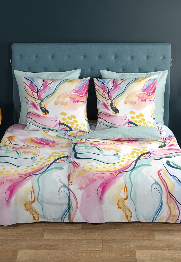 Doppelbett mit türkisfarbenem gepolstertem Kopfende, zwei großen Kissen mit floralem Muster und passender Bettdecke in Rosa-, Gelb- und Türkistönen.
