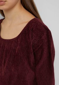 Bordeaux gemêlede top met een vierkante halslijn, verticale ribbels en een zachte, pluche stof; details zijn onder andere licht gepofte mouwen.