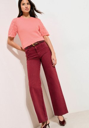 Rožinis megztas viršus su tekstūruotomis trumpomis rankovėmis, derinamas su bordo aukšto liemens džinsais ir aukštakulniais bateliais. Paprasta diržo detalė juosmens srityje.