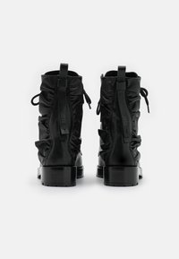 Bottines en cuir noir avec un design froncé, talon plat et languettes en tissu. Texture lisse avec un style minimaliste.