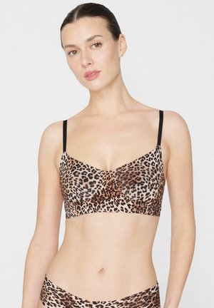 Frau trägt Leopardenmuster-BH und passende Unterwäsche, steht vor einem schlichten weißen Hintergrund mit neutralem Gesichtsausdruck.