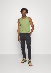 Grøn ærmeløs træningstop, sorte tapered joggingbukser og gule løbesko med røde accenter, der har et slankt design og letvægtsmateriale.
