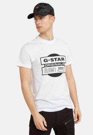 Witte t-shirt met zwarte bedrukte tekst "G-STAR ORIGINALS RAW DENIM." Zwart camouflage pet met een rechthoekige logopatch. Casual fit.