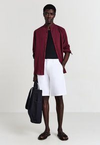 Burgundy textured shirt, black t-shirt, white shorts, and brown sandals. Black tote bag with shoulder strap and front pocket.