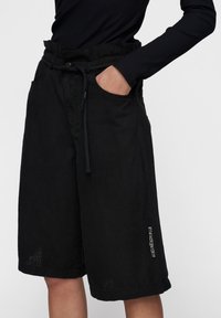 Zwarte linnen shorts met een elastische tailleband, zijzakken en een subtiele witte print op het linkerpoot. Lichtgewicht stof met een gestructureerde uitstraling.