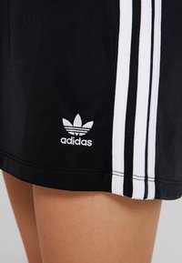 Černé sportovní šortky s bílým třípruhovým designem, vyrobené z texturované tkaniny. Obsahují vyšívané bílé logo Adidas na lemu.